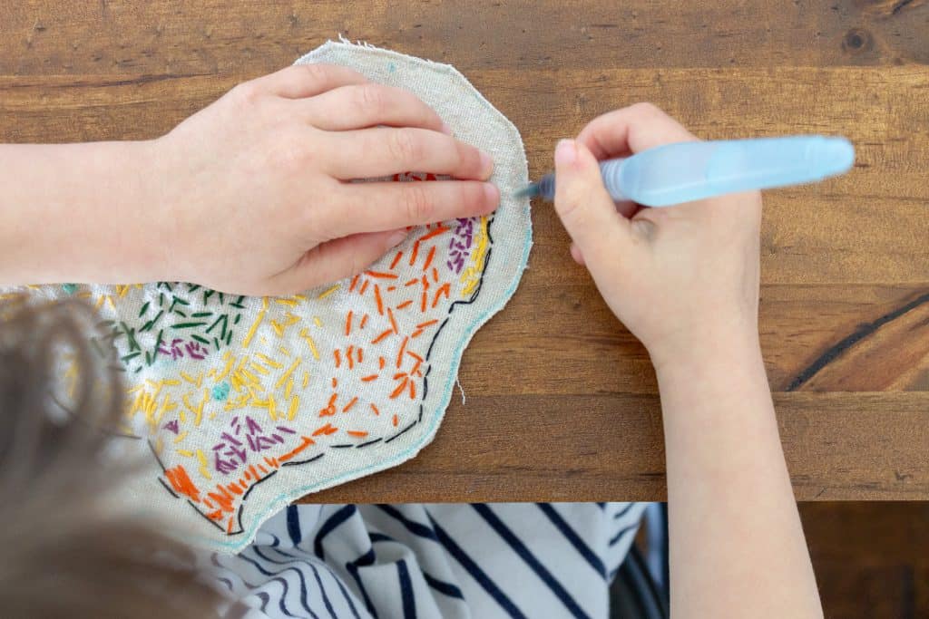 The embroidered map of the biomes of Africa has been sewn and cut out. A young girl now uses a water brush to erase the last fabric market template lines. 